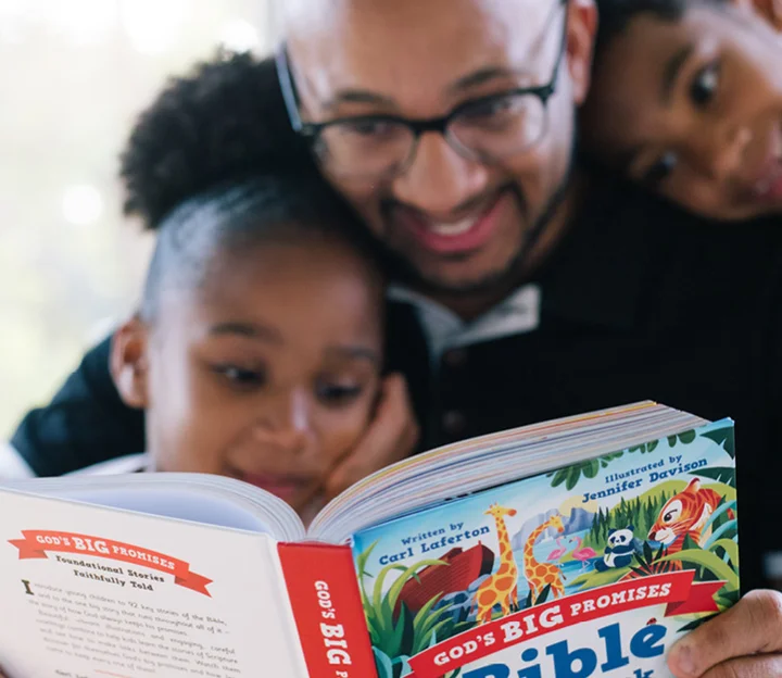 A father and two children are gathered around reading God's Big Promises Bible Storybook